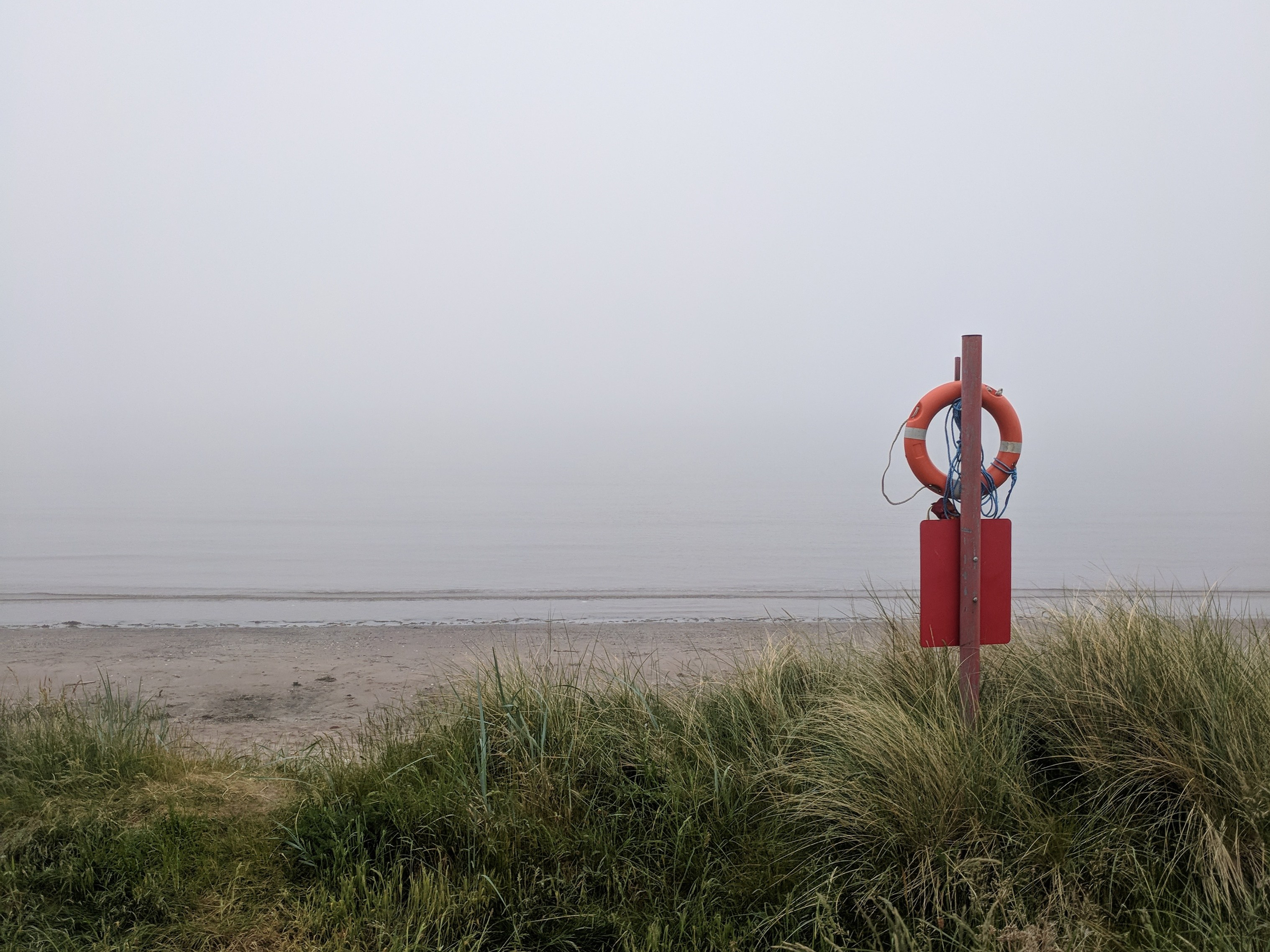 A misty beach viewed from the dunes with a life belt on a pole